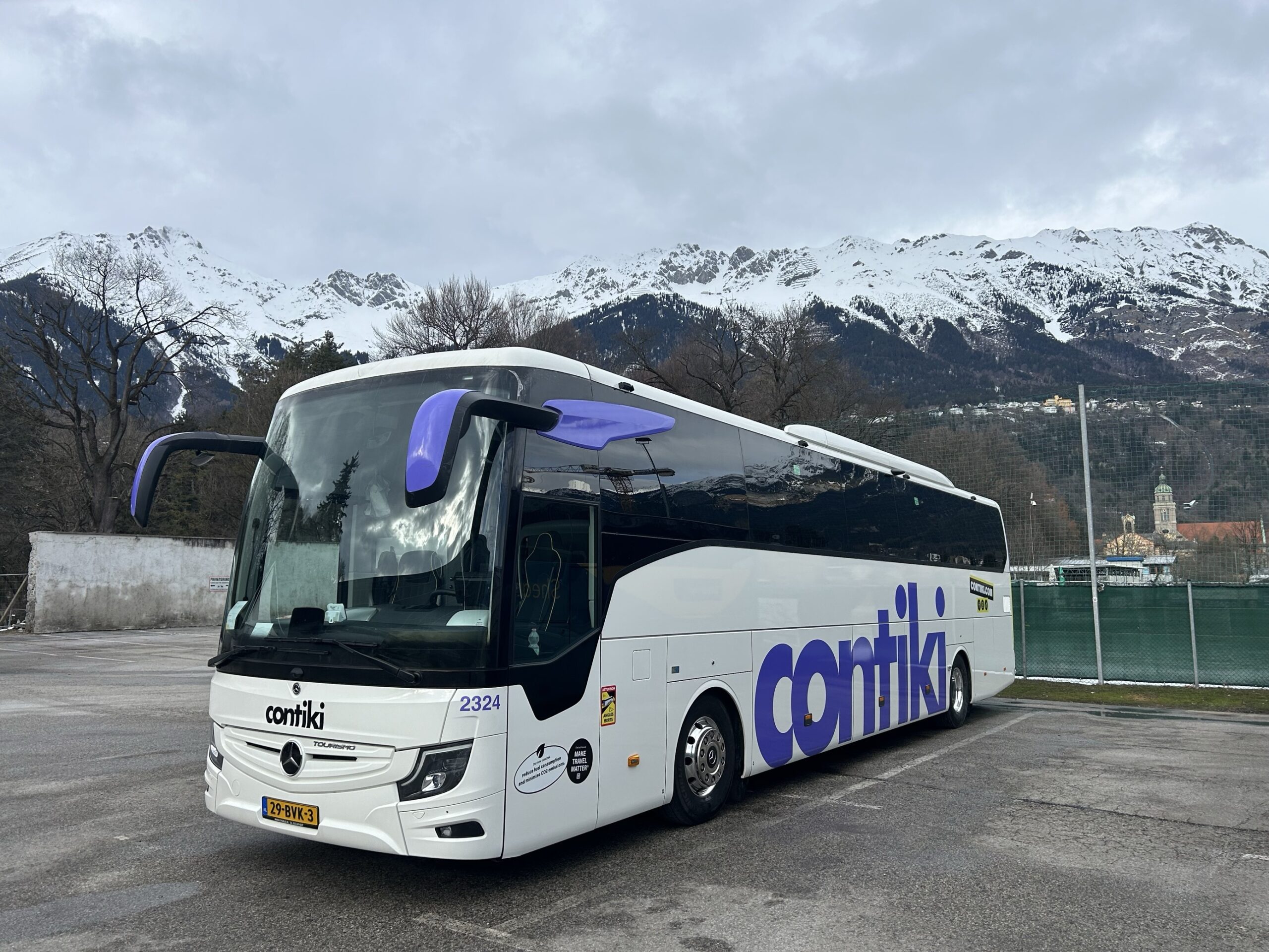 Contiki Coach parked in car park with snowy mountain behind- grey weather