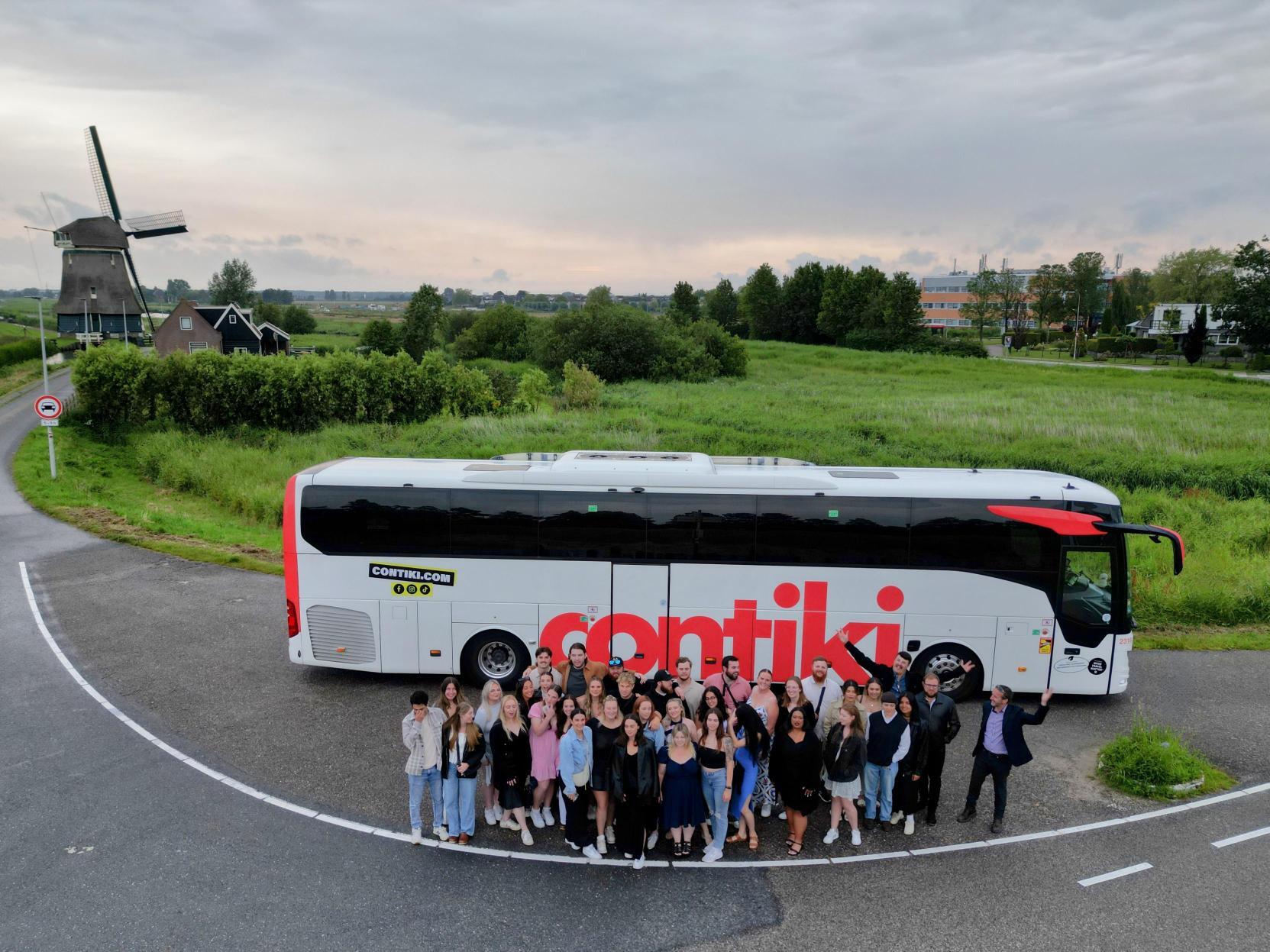 Contiki coach parked with windmill behind and a group of people in front in Holland